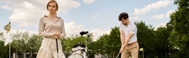 Młoda para w stylowym stroju gra w golfa w parku, ciesząc się spokojnym dniem spędzonym razem na zielonym. - Zdjęcie, obraz