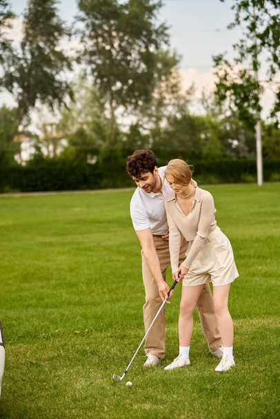 Un hombre y una mujer con elegante atuendo juegan al golf en un amplio campo verde en un prestigioso club de campo. - Foto, Imagen