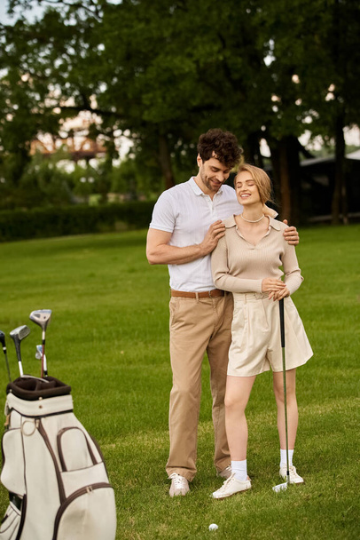 Zarif giyinmiş şık genç bir çift yemyeşil bir golf sahasında yan yana durur.. - Fotoğraf, Görsel