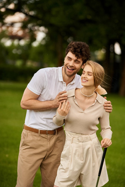 Un hombre y una mujer con estilo posan en un pintoresco entorno de parque, encarnando sofisticación atemporal y romance. - Foto, Imagen
