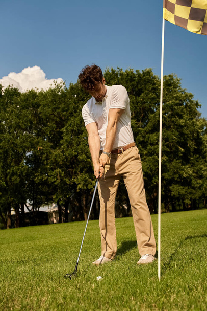 エレガントな服装の男がゴルフクラブをスイングし,ゴルフクラブで芝生場でボールを打つ. - 写真・画像