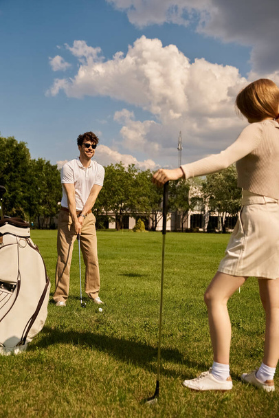Una giovane coppia vestita elegantemente giocare a golf insieme in un parco, godendo di una piacevole giornata all'aria aperta. - Foto, immagini