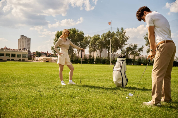 Ένας κομψός άντρας και γυναίκα απολαμβάνουν ένα παιχνίδι γκολφ σε ένα όμορφο πράσινο γήπεδο, που περιβάλλεται από τη φύση και τον καθαρό αέρα. - Φωτογραφία, εικόνα