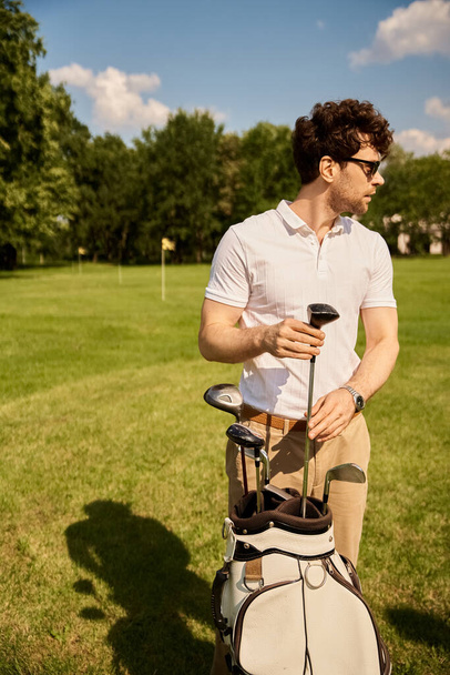 Stylowy mężczyzna z torbą golfową na spokojnym polu golfowym, ucieleśniający elegancję stylu życia wyższej klasy. - Zdjęcie, obraz