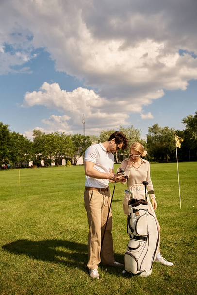 Una joven pareja, vestida con un elegante atuendo, se encuentra en un exuberante campo de golf verde disfrutando de un momento juntos. - Foto, Imagen