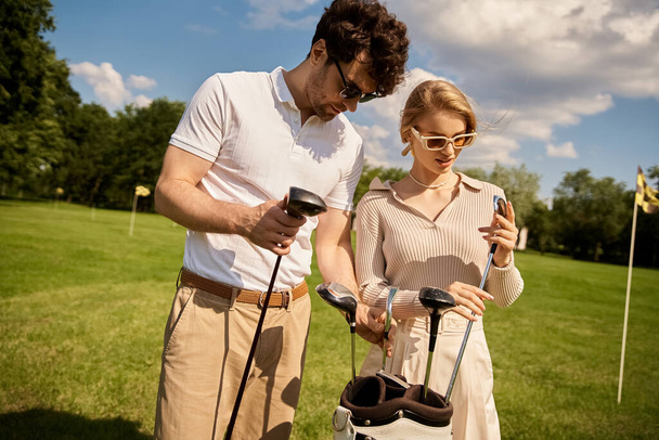 A young couple in elegant attire enjoying a game of golf on a lush green field at a prestigious golf club. - Photo, Image