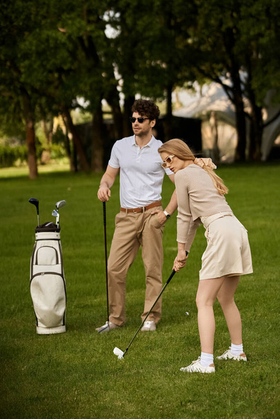 Egy fiatal férfi és nő elegáns ruhában golfoznak egy zöld mezőn egy parkban, egy klasszikus felső osztálybeli életstílust testesítve meg.. - Fotó, kép