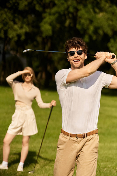 Een stijlvolle man en vrouw die golfen in een park, genieten van een ontspannen ronde op een zonnige dag. - Foto, afbeelding
