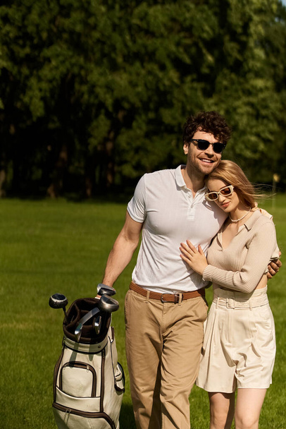 Um homem e uma mulher vestidos elegantemente posam para uma foto em um campo de golfe verde exuberante, desfrutando de um dia sofisticado. - Foto, Imagem