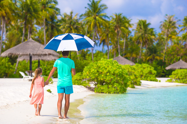 Vater und kleines Mädchen mit Regenschirm verstecken sich vor Sonne am Strand - Foto, Bild