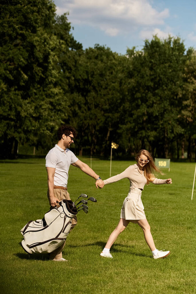 A stylish couple in elegant attire hold hands while walking leisurely on a manicured golf course. - Photo, Image