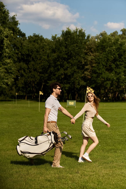 Zarif bir şekilde giyinmiş şık genç bir çift, klasik karmaşıklığın göstergesi olarak yemyeşil bir golf sahasında el ele yürürler.. - Fotoğraf, Görsel