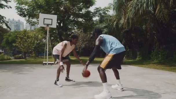 Breed schot van mannelijke atleet doen steeg-oop met bal tijdens het spelen van streetball met een vriend op outdoor speeltuin - Video