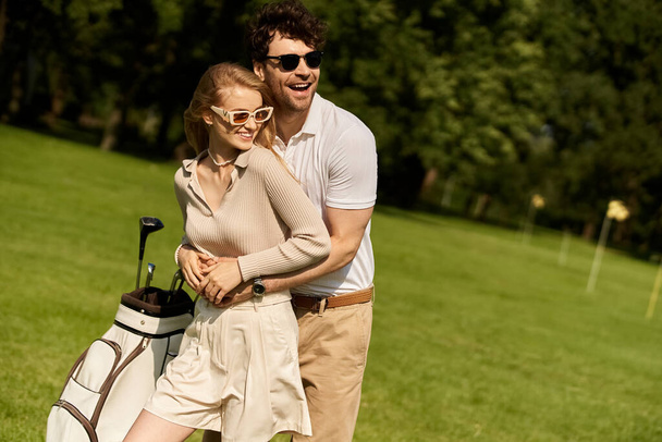 Egy fiatal férfi és egy nő elegáns öltözékben osztoznak egy pillanatnyi szereteten, miközben egy buja zöld golfpályán pózolnak.. - Fotó, kép