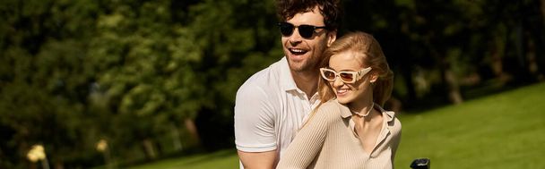 Un uomo e una donna elegantemente vestiti abbracciando in un parco, godendo di una piacevole attività all'aperto insieme. - Foto, immagini