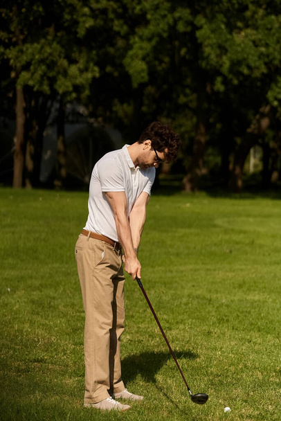 Egy férfi elegáns öltözékben lengeti a golfütőt, üti a labdát egy buja zöld parkban, élvezi a luxus sport tevékenységet. - Fotó, kép