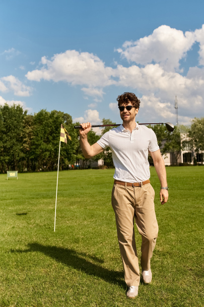 Nuori mies tyylikkäässä puvussa seisoo nurmikentällä, pitäen golfmailaa hienostuneesti ja tyylikkäästi. - Valokuva, kuva
