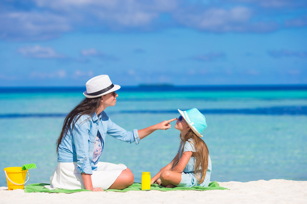 Mãe aplicando creme de proteção solar para sua filha na praia tropical
 - Foto, Imagem