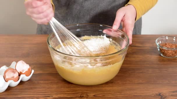 En un tazón de vidrio, un batidor de mano grande mezcla expertamente los ingredientes para un delicioso pastel de pan de jengibre con glaseado de caramelo. - Metraje, vídeo