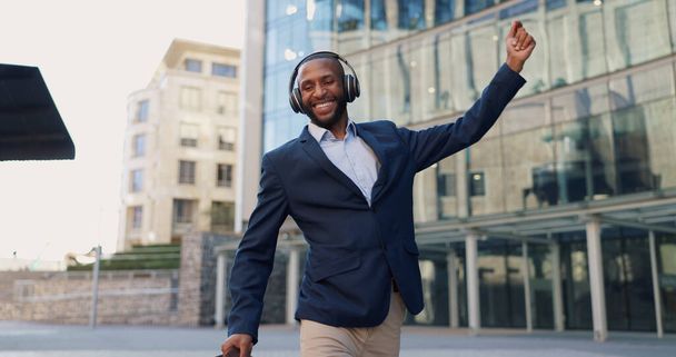 Business man, dancing and headphones in city with smile, steps and spin with bag for commute by office buildings. Person, employee or excited dancer with music, briefcase or outdoor on metro sidewalk. - Photo, Image