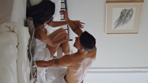 Happy boyfriend jumping wife laying at bed. Carefree sweethearts laughing out loud feeling joyful at weekend apartment vertical view. Pyjamas couple having fun at bedroom interior. Morning activities  - Footage, Video