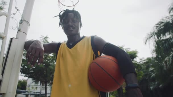 Tieffliegerporträt eines afroamerikanischen Sportlers, der während seines Aufenthalts auf einem Spielplatz im Freien in die Kamera lächelt - Filmmaterial, Video