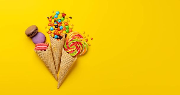 Various colorful candies, lollipops, and macaroons. Flat lay sweets over yellow background with copy space - Photo, Image