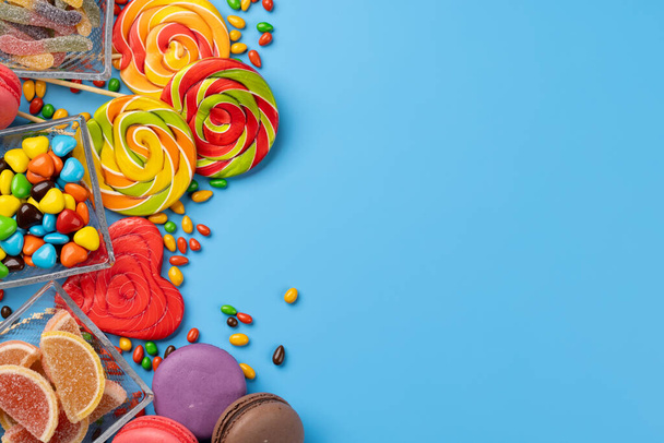 Varie caramelle colorate, lecca-lecca e macaron. Dolci piatti lay su sfondo blu con spazio di copia - Foto, immagini