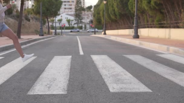 Una mujer cruza un camino de coche en un cruce peatonal con grandes zancadas, filmación en cámara lenta. España, Alicante - Metraje, vídeo