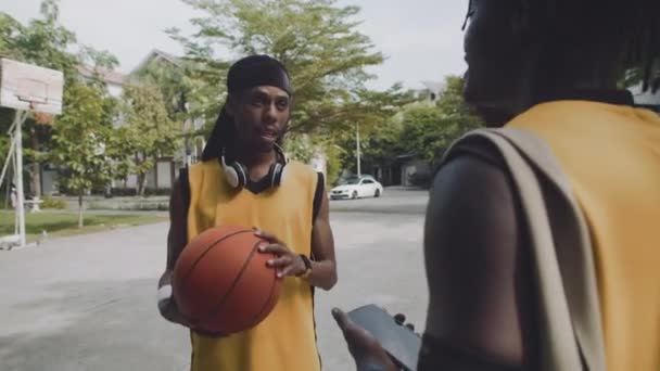 Plan moyen de deux amis noirs masculins se réunissant sur le terrain de jeu de streetball et parlant - Séquence, vidéo