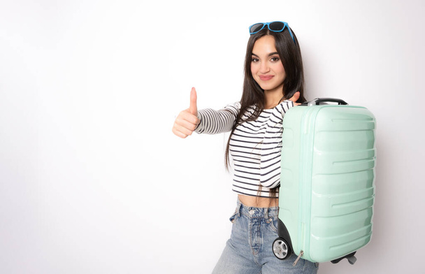 Mujer divertida preparándose para las vacaciones de verano sosteniendo la maleta sobre sus hombros sobre fondo blanco. - Foto, Imagen