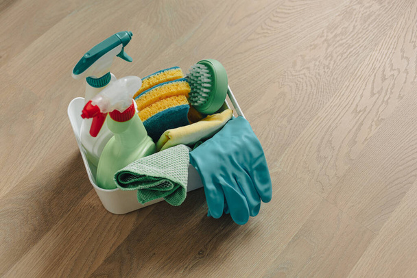 Brushes, bottles with cleaning liquids, sponges, and rubber gloves. Cleaning supplies on wooden floor. - Fotografie, Obrázek