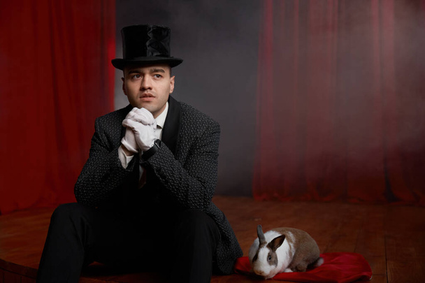 Pensive showman in suit sitting on theatre stage resting after magic festival show. Portrait of relaxed male magician artist after fantasy performance - Photo, Image