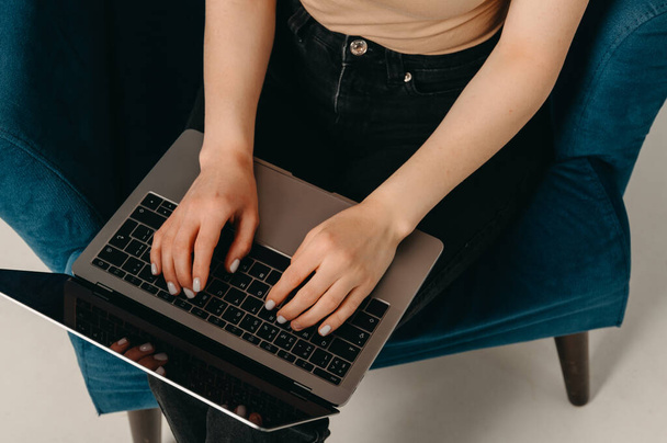 Bezimienne zdjęcie młodej kobiety korzystającej z laptopa podczas siedzenia na niebieskim krześle.  - Zdjęcie, obraz