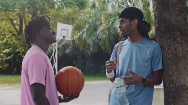Colpo medio di due sportivi neri che salutano dopo l'allenamento di streetball sul campo all'aperto - Filmati, video