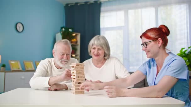 anziano uomo e donna giocare a giochi da tavolo insieme con assistente sociale femminile seduto a tavola - Filmati, video