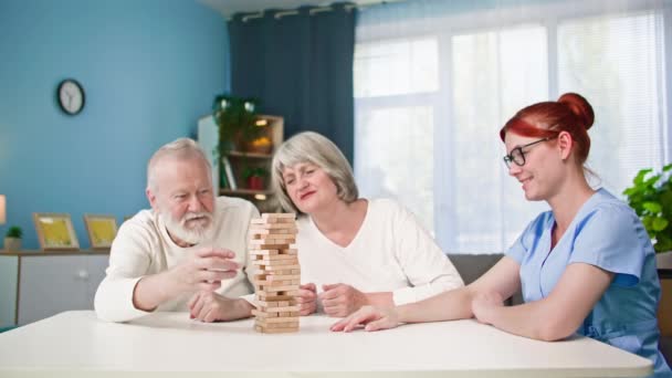 fröhliche Sozialarbeiterin hat Spaß mit alten Männern und Frauen, die Brettspiele spielen, während sie am Tisch sitzen - Filmmaterial, Video