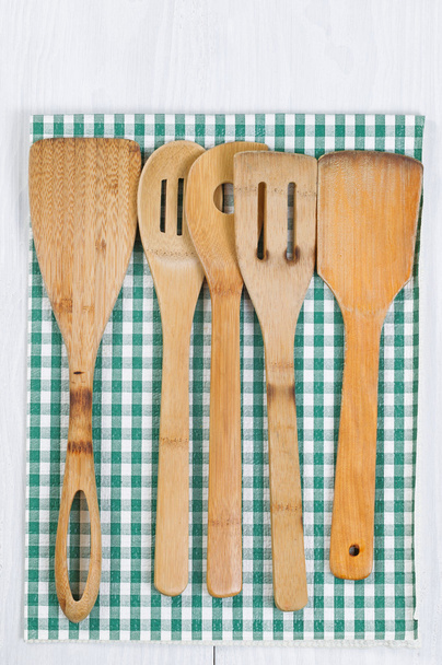 Ξύλινα σκεύη μαγειρικής και πανί χαρτοπετσέτα σε λευκό ξύλο - Φωτογραφία, εικόνα