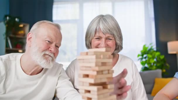 szczęśliwy starszy mężczyzna i kobieta wraz z pracownicą socjalną grając w gry planszowe podczas siedzenia przy stole w pokoju - Materiał filmowy, wideo