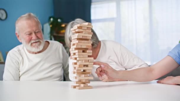 bordspellen, jonge vrouw speelt een spel gemaakt van houten blokken samen met ouderen zitten aan een tafel, - Video