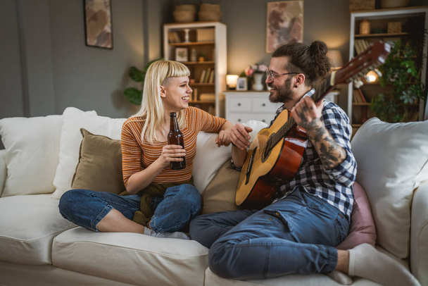 Adult couple enjoy at home play guitar and drink beer happy together - Photo, Image
