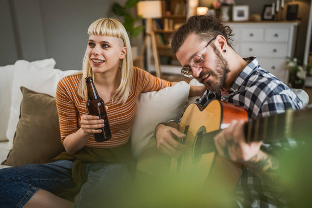 Yetişkin çiftler evde gitar çalıp birlikte mutlu bira içerler. - Fotoğraf, Görsel
