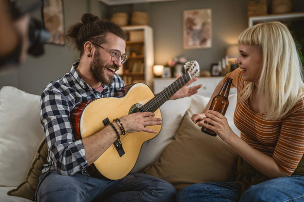Dospělí pár těšit doma hrát na kytaru a pít pivo šťastný spolu - Fotografie, Obrázek