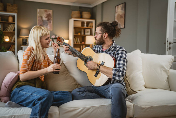 Erwachsenes Paar genießt zu Hause das Gitarrespielen und trinkt glücklich zusammen Bier - Foto, Bild