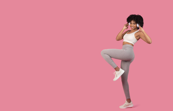 Eine verspielte und energische Afroamerikanerin in sportlicher Kleidung zwinkert und posiert in einem lustigen, isolierten Kleid auf rosa Hintergrund - Foto, Bild