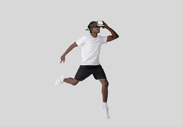 Захоплений афроамериканський хлопець відчуває віртуальну реальність, зображуючи сучасний перетин спорту і технологій, ізольований на звичайному тлі - Фото, зображення