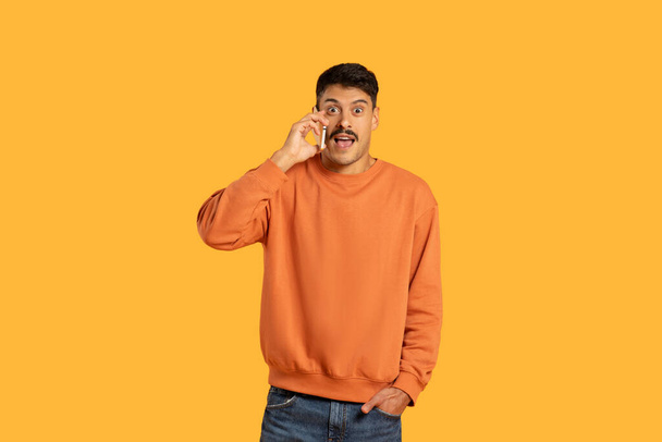 Um cara milenar com um bigode exibe uma expressão engraçada, mas chocada, enquanto isolado em um fundo laranja - Foto, Imagem