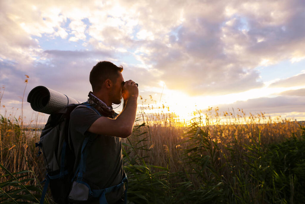 Männlicher Tourist mit Rucksack und Fernglas bei Sonnenuntergang im Feld - Foto, Bild