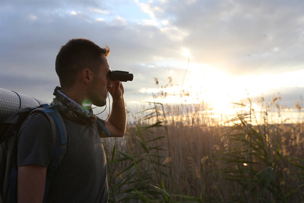 Männlicher Tourist mit Rucksack und Fernglas bei Sonnenuntergang im Feld - Foto, Bild