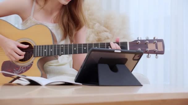 Szoros kéz nő ül kanapén látszó tabletta és össze egy dalt gyakorolni zene gitár a nappaliban, nő nézi leckét online a zene és a tanulás gitár, életmód koncepció. - Felvétel, videó